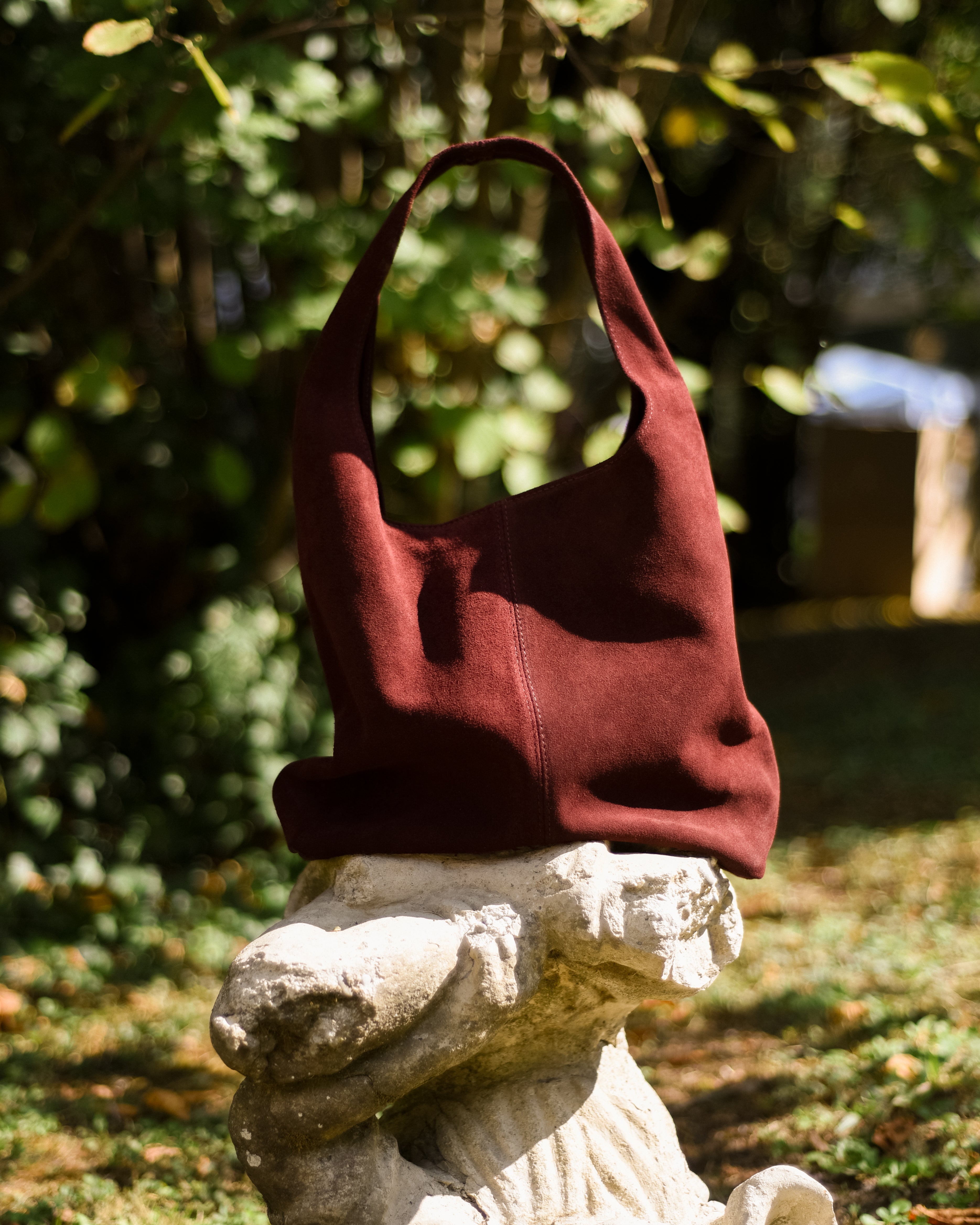 Red handbag on a stone sculpture with greenery in the background
